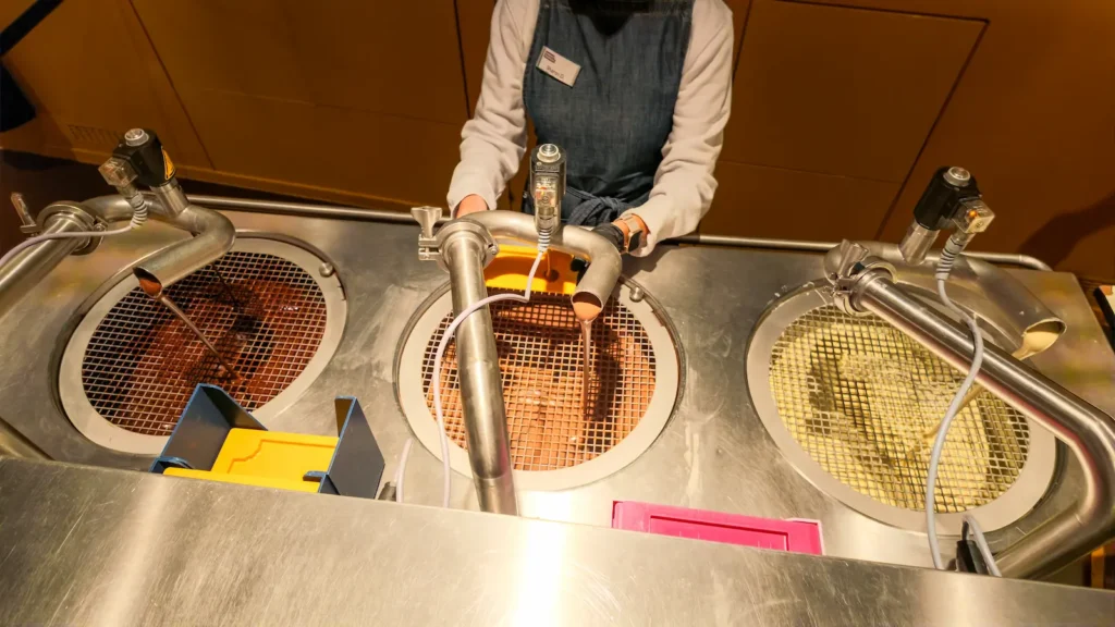 Chocoversum Mould Pour 16x9 Milk, dark and white chocolate being poured into moulds during the chocolate-making workshop at CHOCOVERSUM Hamburg.